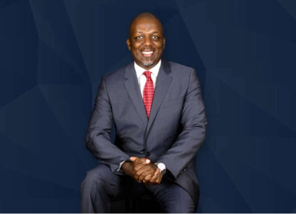 Man in a suit smiling against a dark blue background.