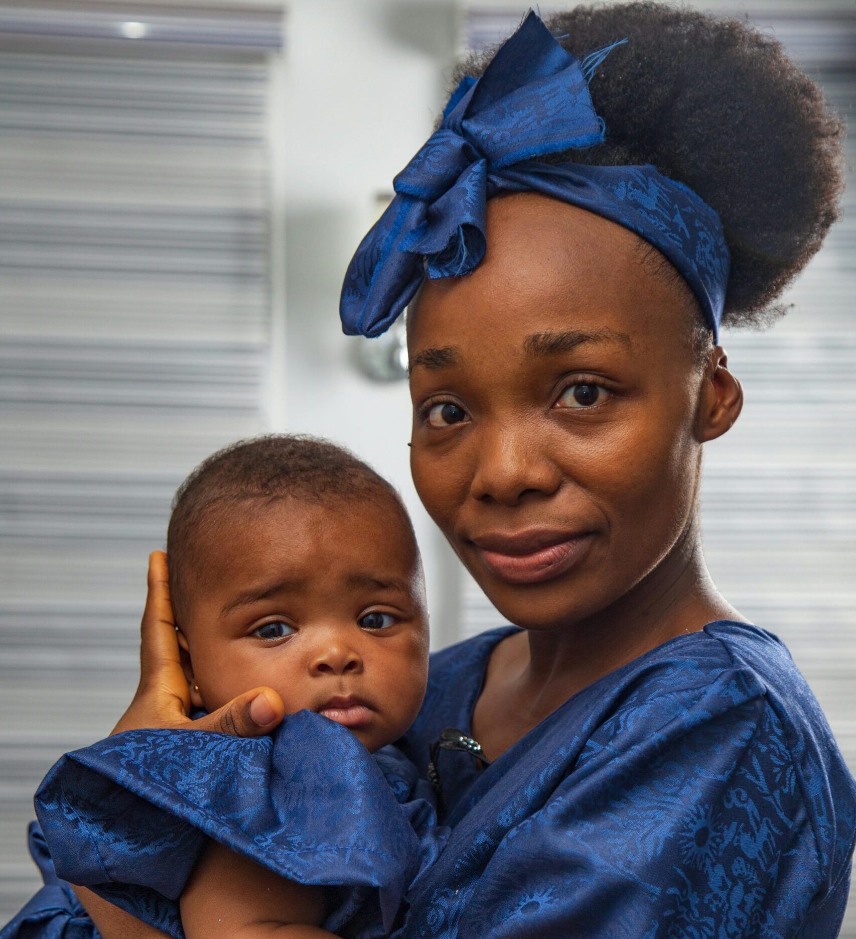 Portrait of a mother holding her baby, both wearing matching blue attire, indoors.